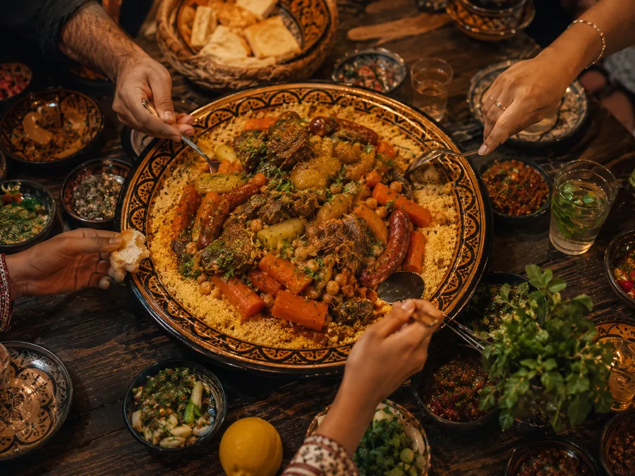 Hands reaching in from every side of one big couscous platter
