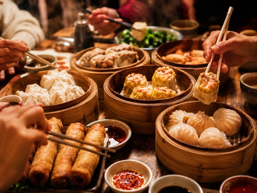 Steaming bamboo baskets of dim sum and spring rolls, chopsticks reaching in
