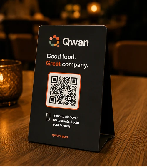 Charcoal table tent carrying the Qwan QR code, lit by a candle